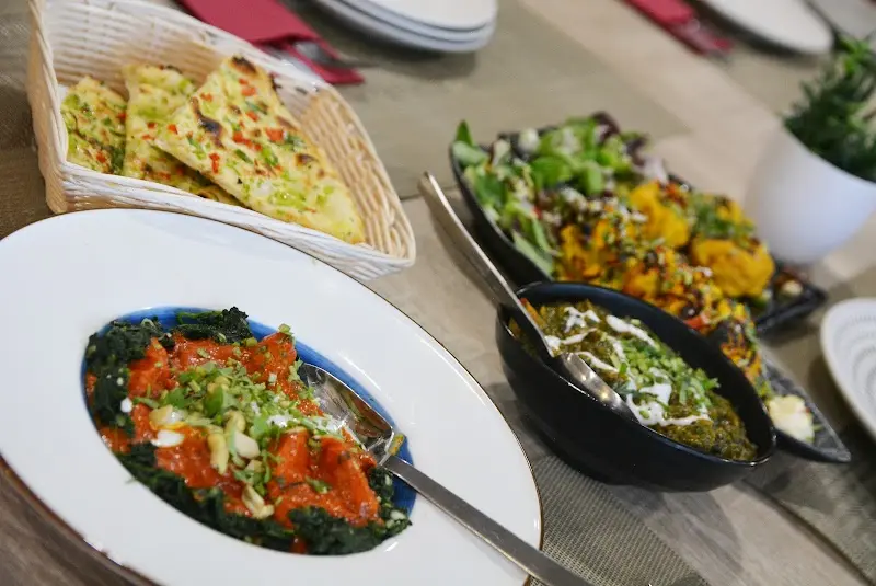 Curris indios con espinacas, cesta de pan naan con ajo y cebolla frita en la mesa