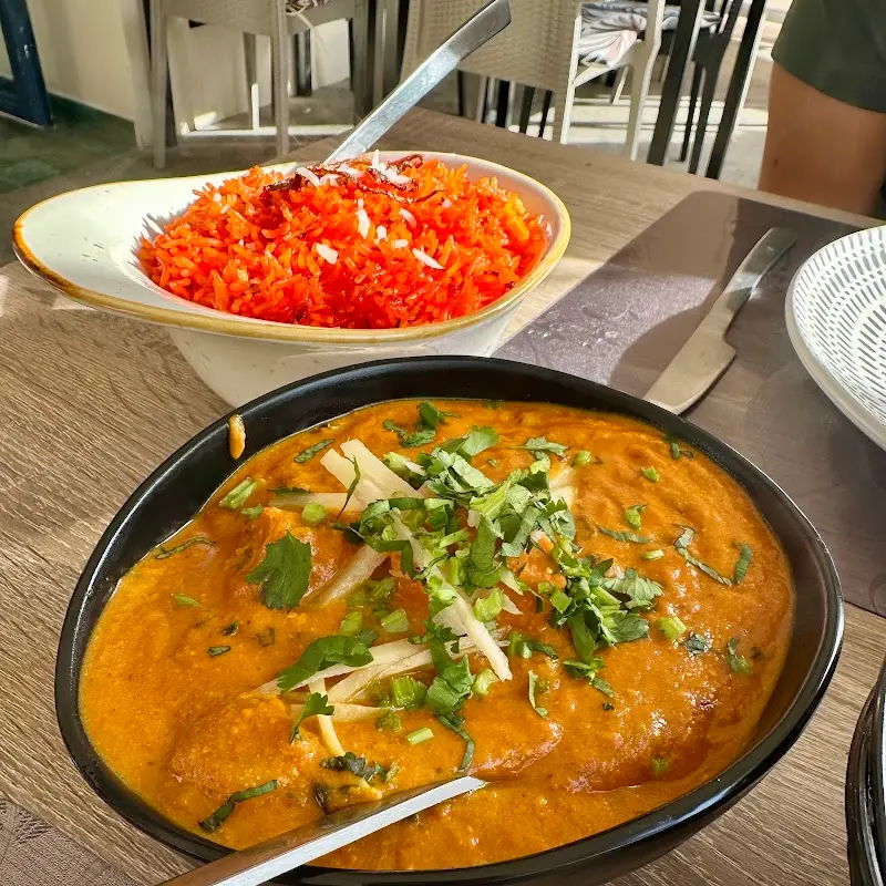 Curry de salsa anaranjada con jengibre y cilantro junto a un cuenco de arroz de colores