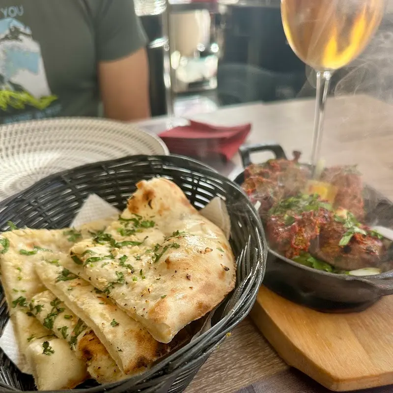 Cesta de pan naan con perejil y carne humeante en una sartén de hierro