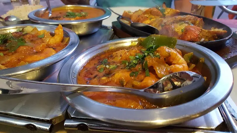 Curry de gambas en cuenco metálico junto a otros currys y pollo tandoori en plancha