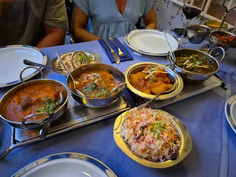 Mesa con varios currys en cuencos metálicos y arroz pilaf con verduras en un restaurante indio