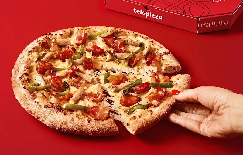 Pizza con bacon, salchichas y pimiento verde junto a su caja roja de reparto