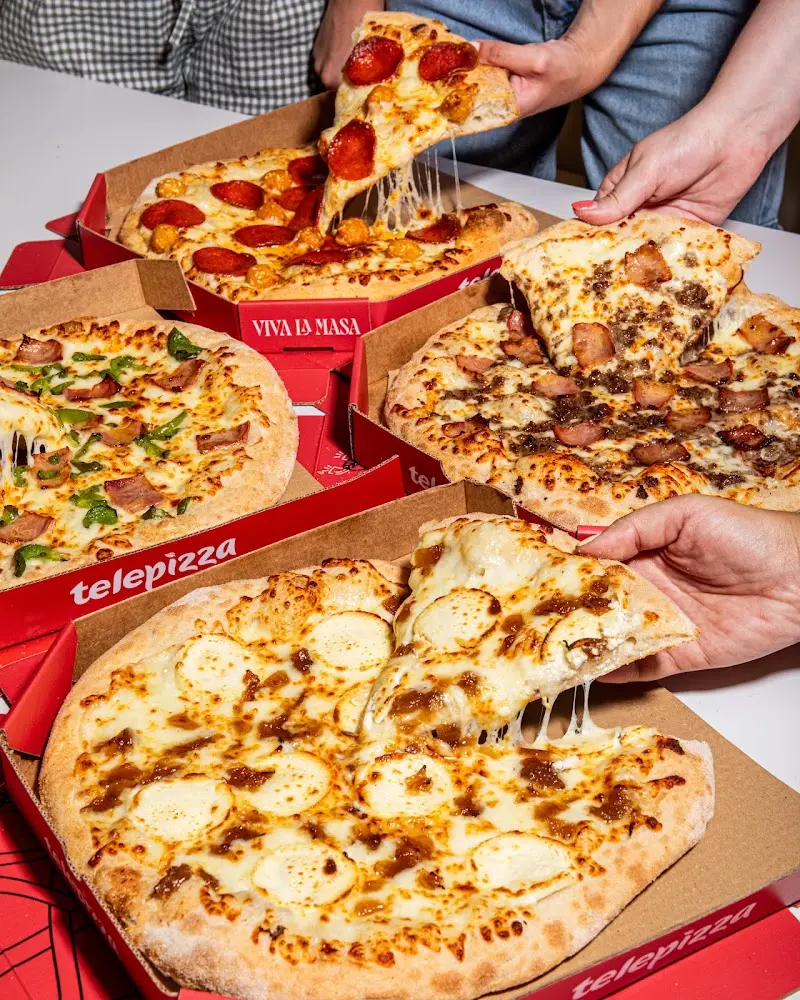 Varias pizzas en sus cajas de Telepizza mientras se sirven porciones con queso fundido