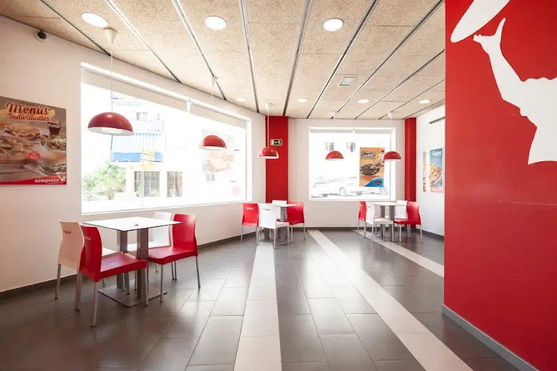 Comedor del local con mesas blancas, sillas rojas y lámparas colgantes