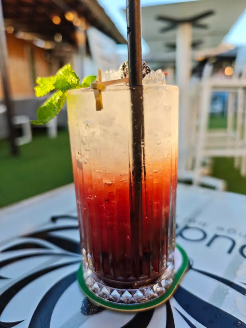 Cóctel rojo degradado con hielo, menta y pajita sobre una mesa de la terraza