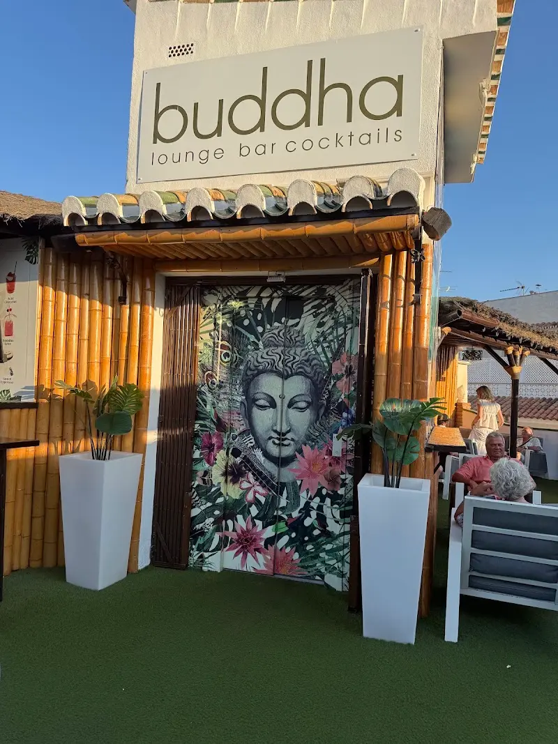 Entrada de bambú con puerta decorada con un Buda entre flores y el rótulo del local