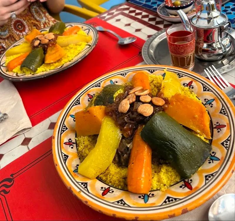 Cuscús con verduras, cebolla caramelizada y almendras en plato pintado, junto a té moruno