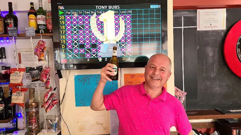 Un jugador celebra con una cerveza ante la pantalla de resultados de dardos