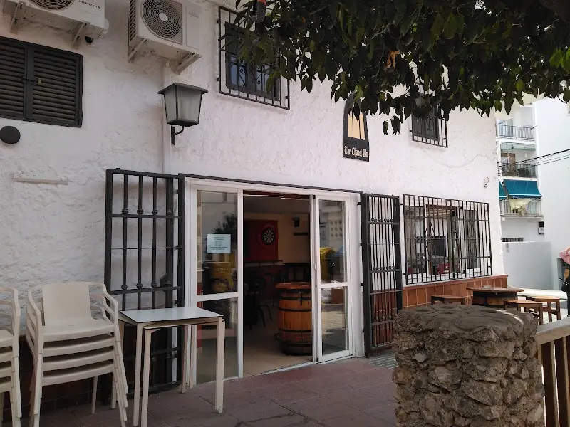 Entrada de La Capilla con rejas abiertas, mesas plegadas y diana al fondo