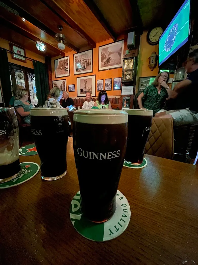 Pintas de Guinness en la barra con clientes y paredes llenas de cuadros al fondo