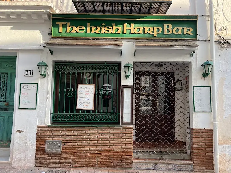 Fachada del pub con letrero verde y dorado y la persiana metálica bajada de día
