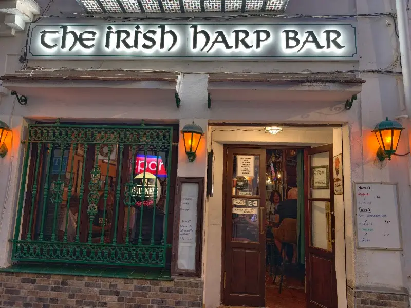 Letrero iluminado de The Irish Harp Bar de noche, con farolillos y la puerta abierta