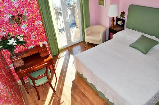 Habitación con papel pintado de flores, escritorio antiguo, butaca y cama de matrimonio