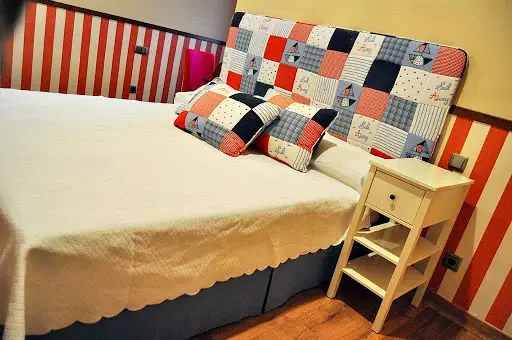 Cama con cabecero de patchwork marinero, cojines a juego y paredes de rayas rojas