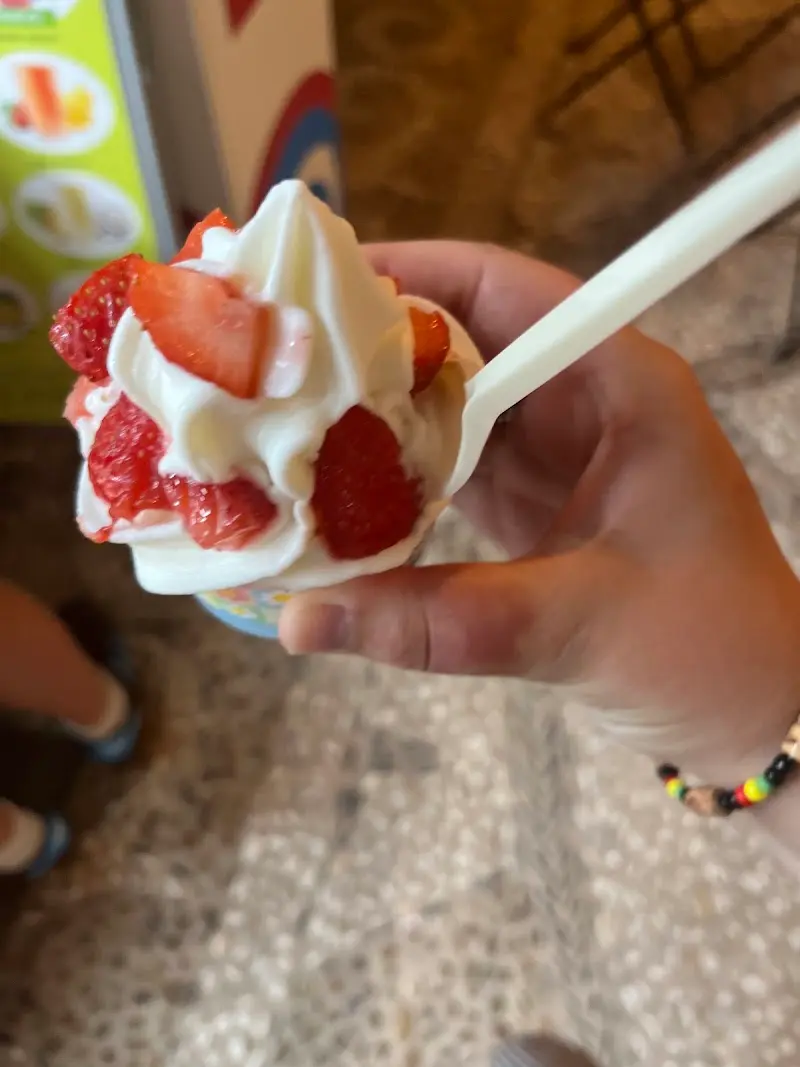 Yogur helado con fresas troceadas y cucharilla en la mano de un cliente