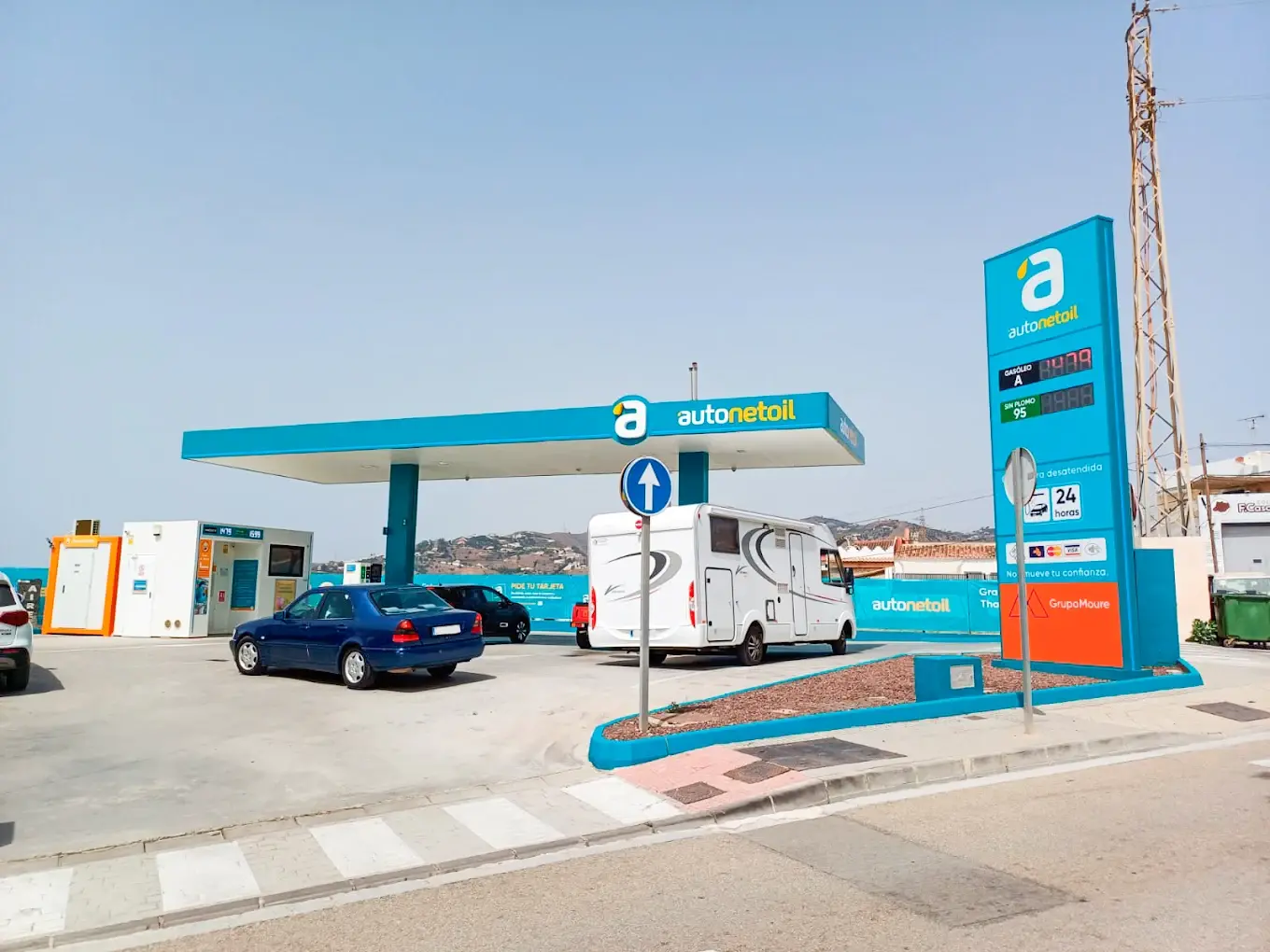 Entrada a la gasolinera con el monolito de precios, una autocaravana y la sierra al fondo