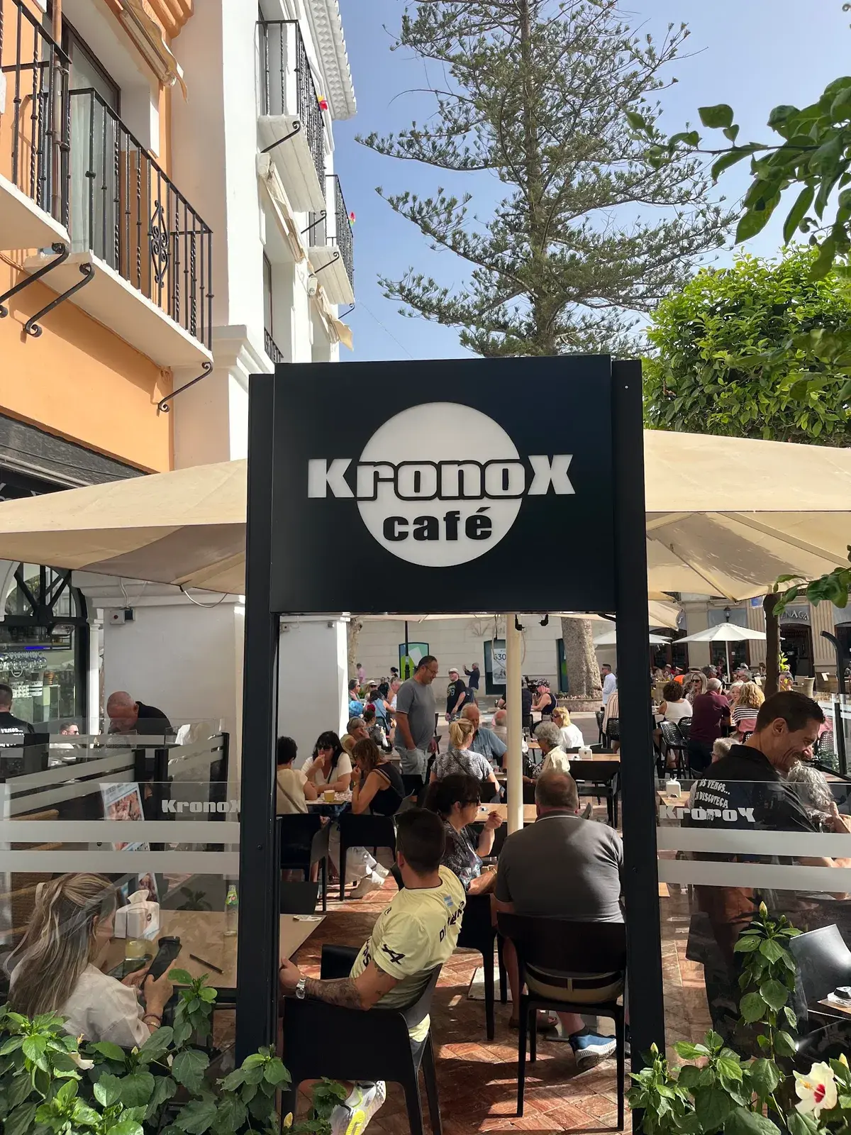 Cartel de Kronox Café a la entrada de su terraza llena de clientes