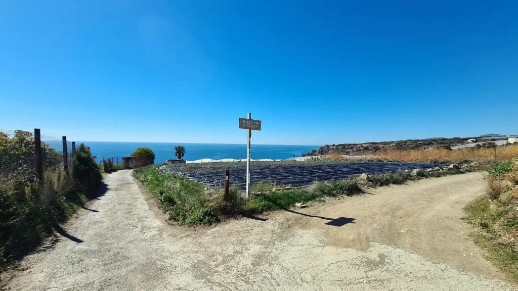 Poste que indica el camino a la playa La Caleta entre los invernaderos de Maro